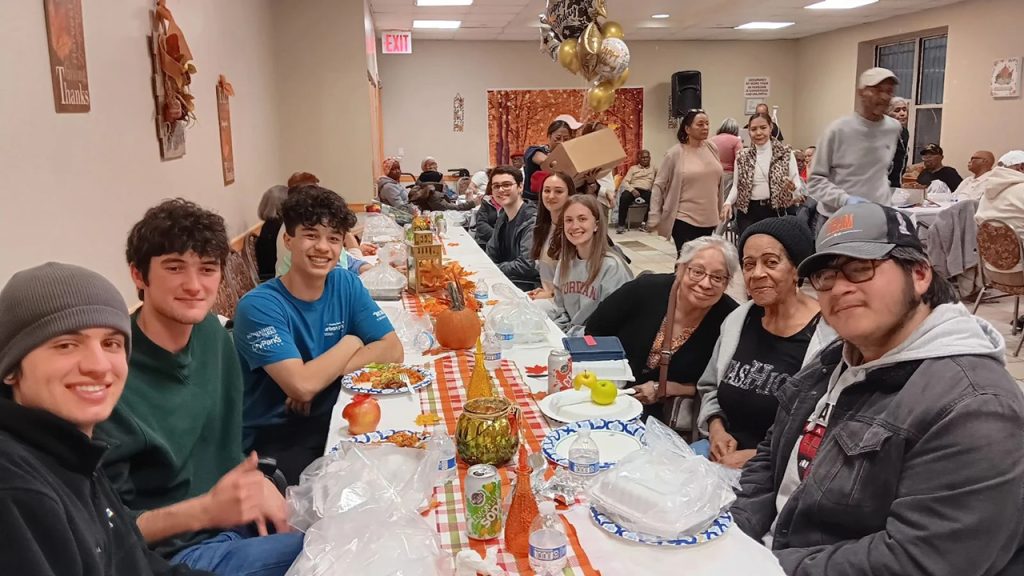 Thanksgiving Spirit: A Bronx Turkey Giveaway Students join senior citizens at a Thanksgiving dinner at a long table