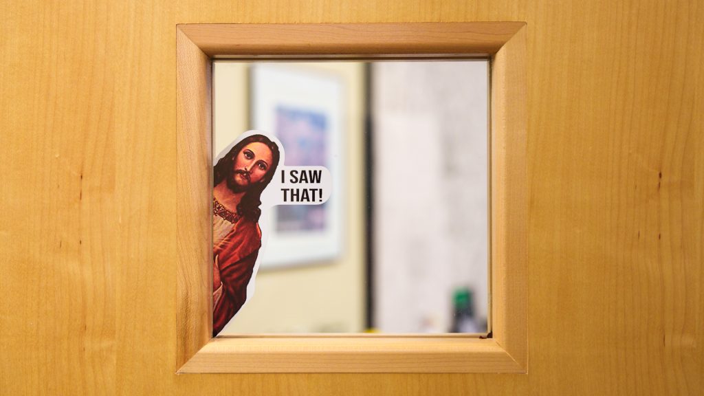 A window in a door, featuring a sticker of Jesus with the phrase "I SAW THAT!" 