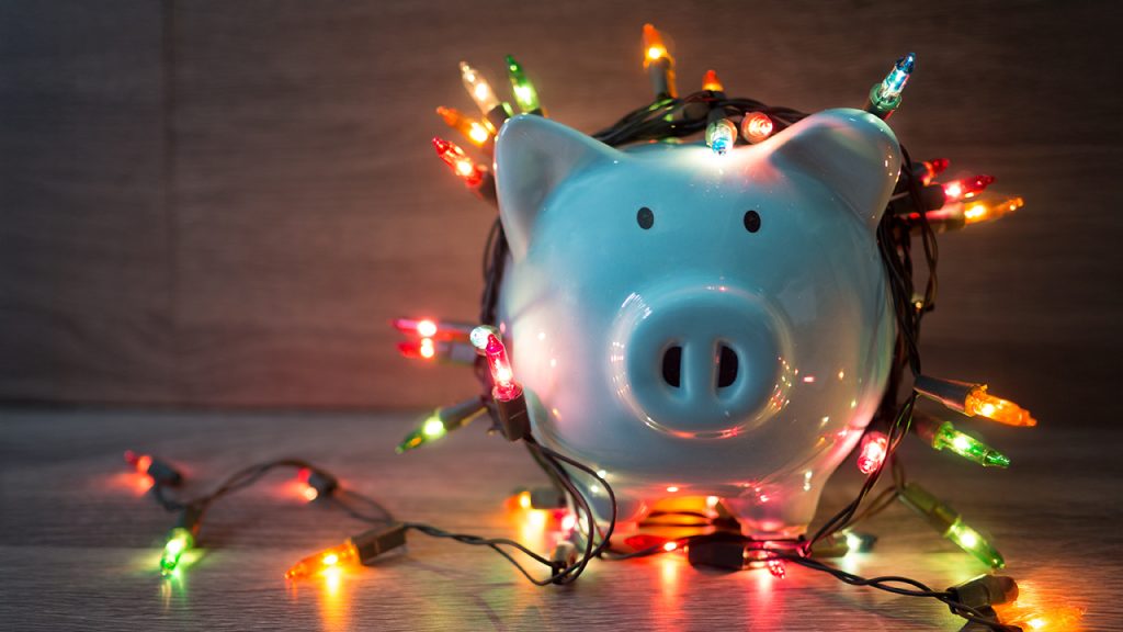 How to Control Your Spending This Holiday Season: 6 Research-Backed Tips An image of a piggy bank draped in Christmas lights