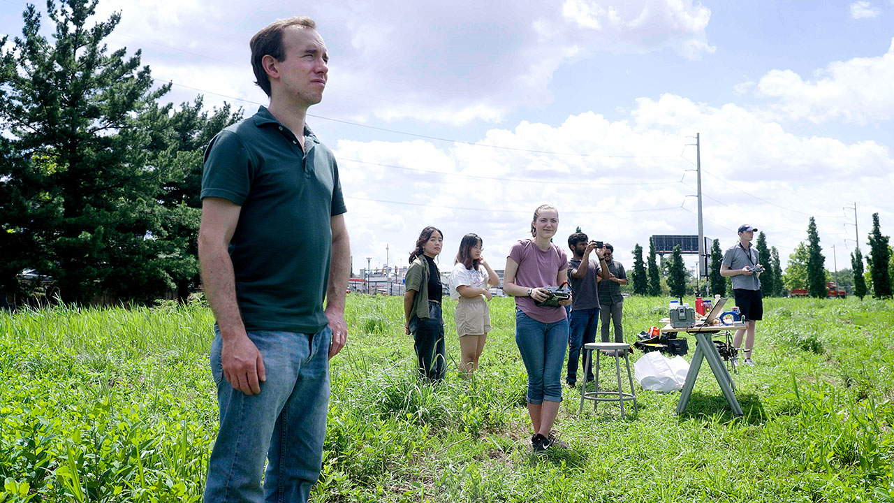 UPenn Team PRONTO members stand in a field with robot controls
