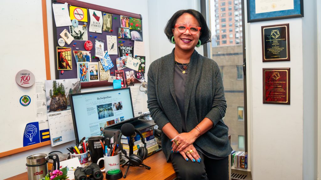 What’s on My Desk: Christina Greer Christina Greer sits on the edge of her desk in her office and smiles at the camera.