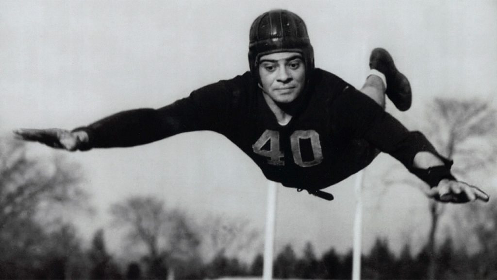 Fordham football player Vince Lombardi soars through the air, arms outstretched, in this publicity photo from 1936.