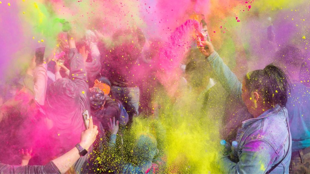 An image of a Holi celebration with participants tossing colorful powders into the air