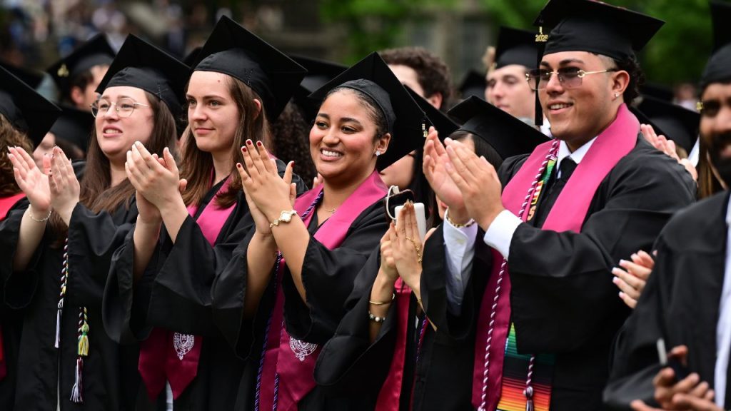 An image of members of Fordham's class of 2025 at commencement, clapping in their caps and gowns.