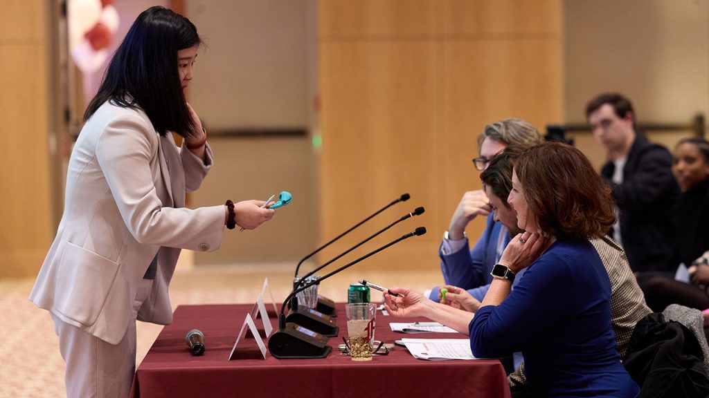 A woman hands a plastic tool to three people seated at a table.