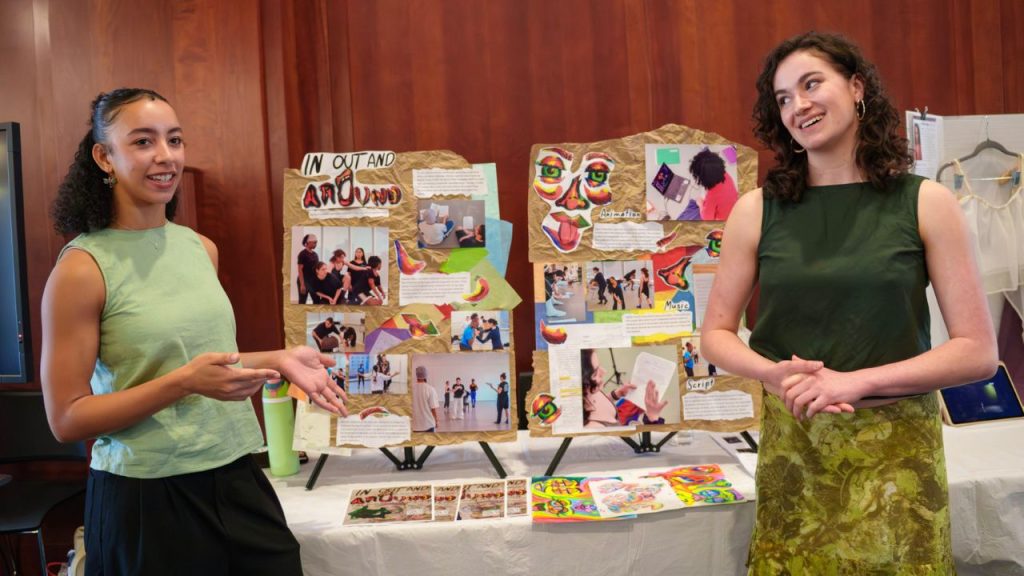 Two women stand in front of a poster board presenting a dance project