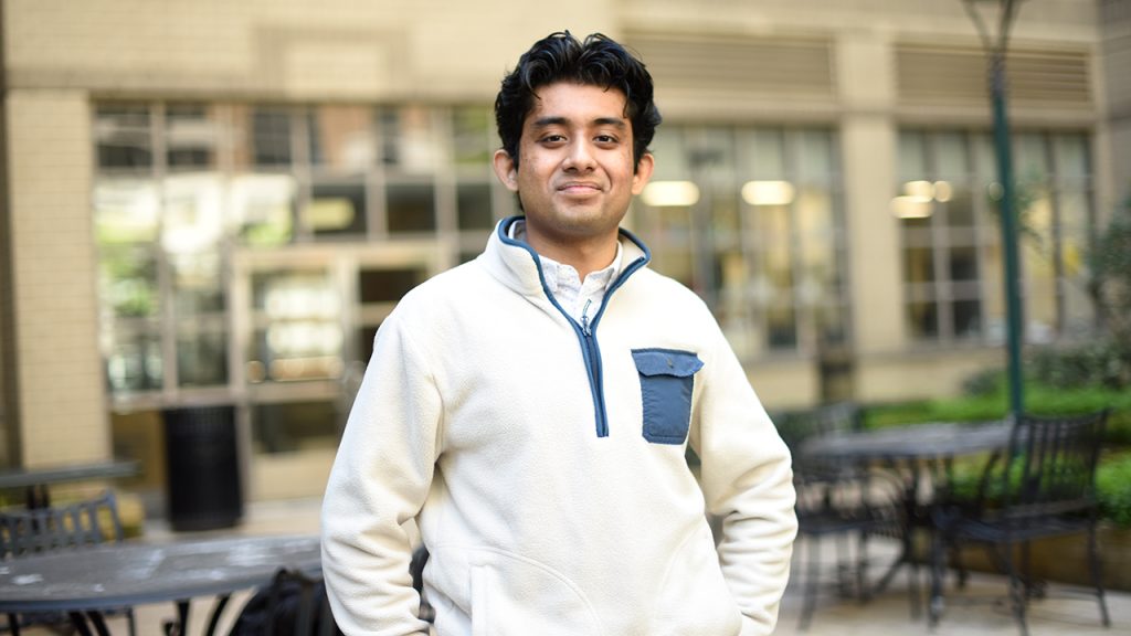 Man student standing in outdoor area with tables and chairs
