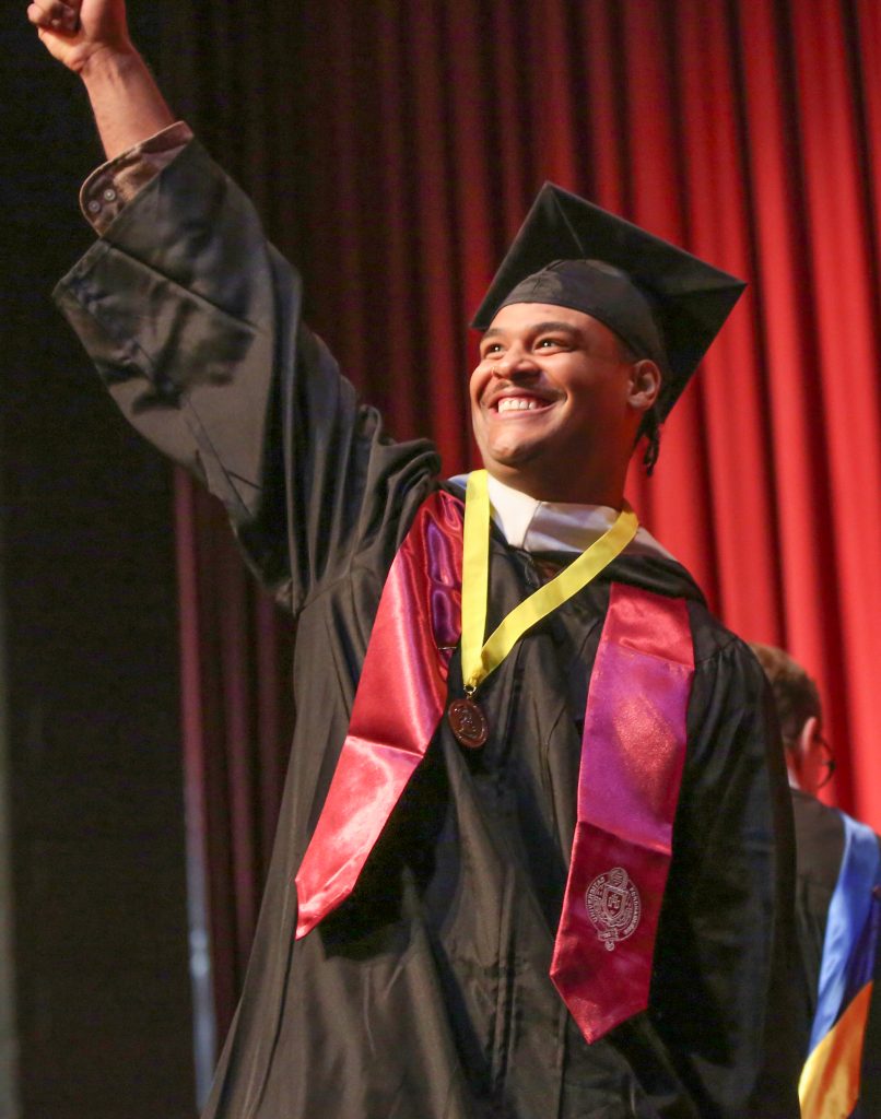 A PCS graduate waving to the audience from the stage