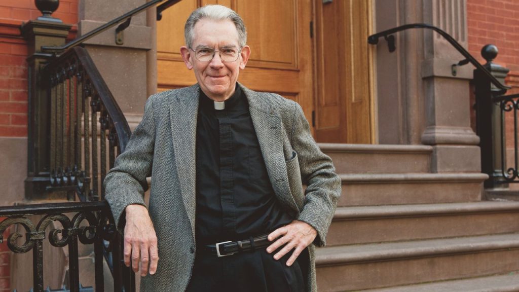 A photo of Father Joseph Parkes posing in front of a brownstone stoop.