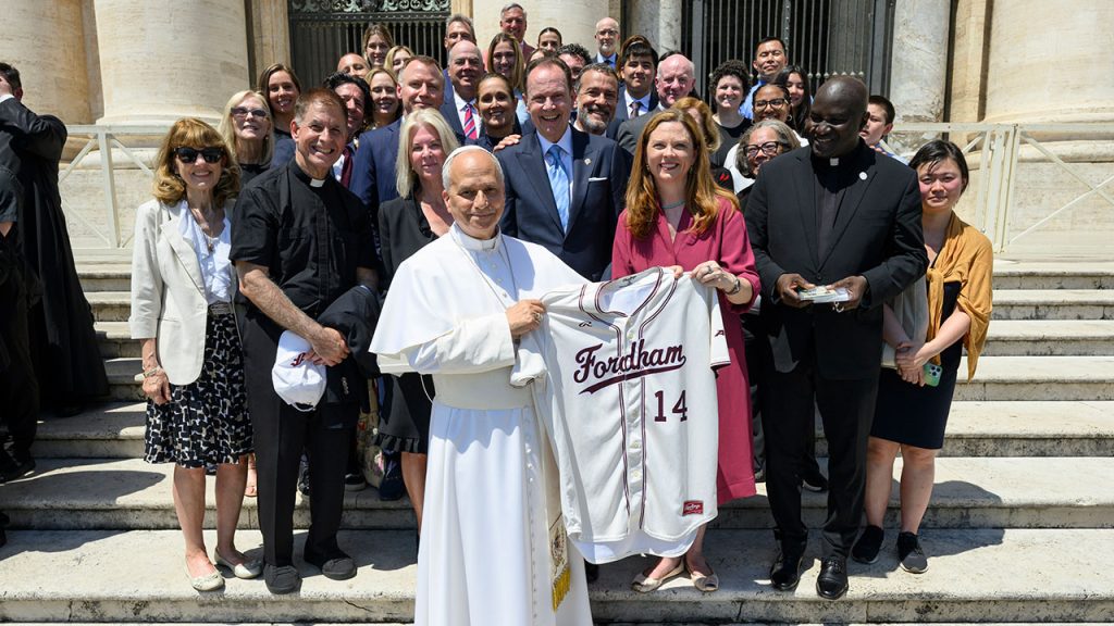 A Fordham delegation with Pope Leo holding a Fordham jersey at the Vatican