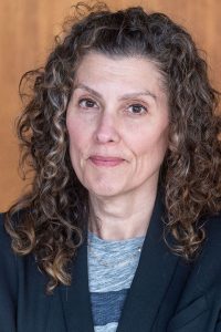 Headshot of Lauri Goldkind with curly hair, wearing a dark blazer over a gray and blue top