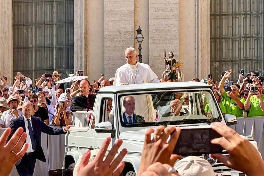 The pope smiles at a crowd of people from the Popemobile.