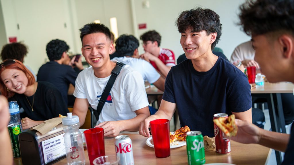 Students smiling and eating together during a pizza lunch for incoming international students.