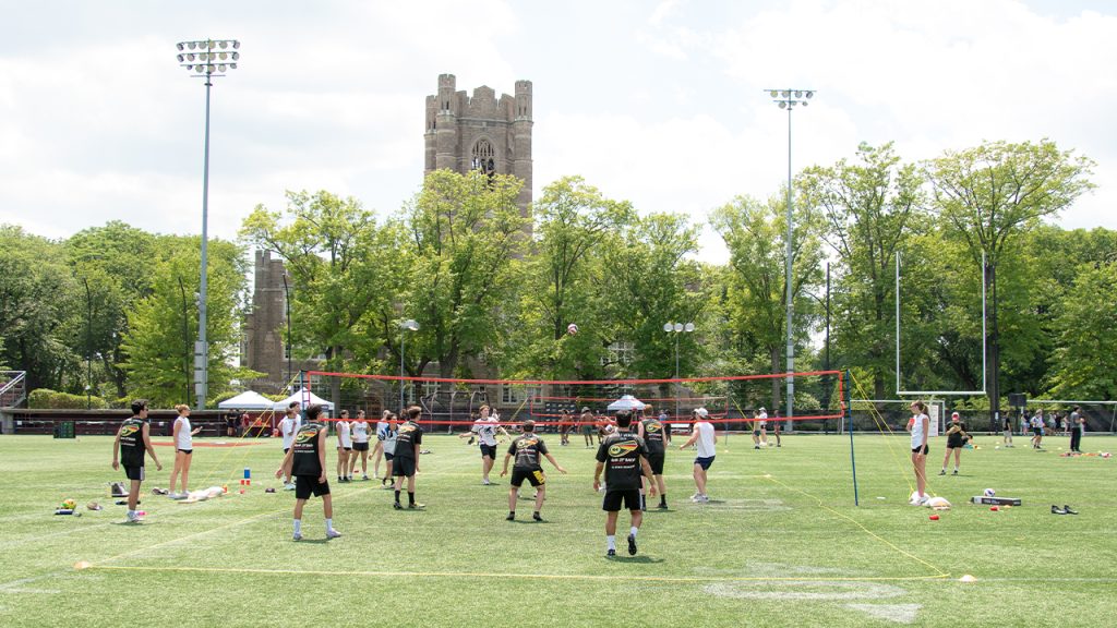 A volleyball game on the Moglia Stadium field with Keating Hall in the background