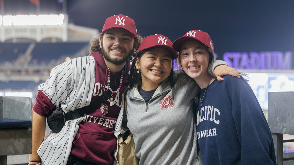 three young adults in Fordham gear at Yankee Stadium