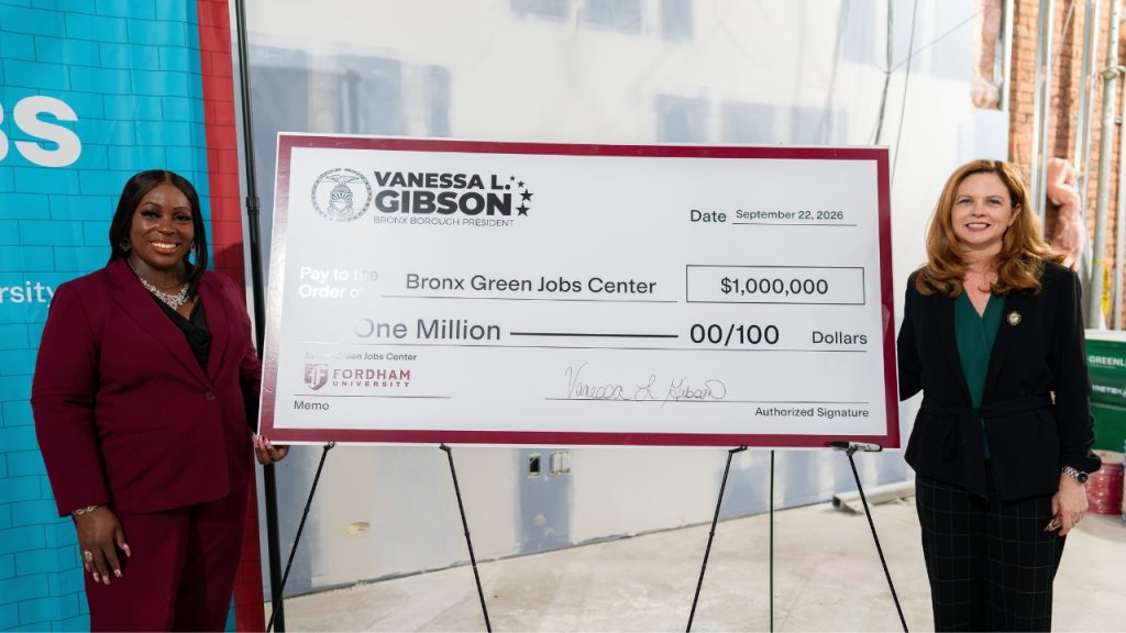 Two women standing on either side of a giant check for one million dollars