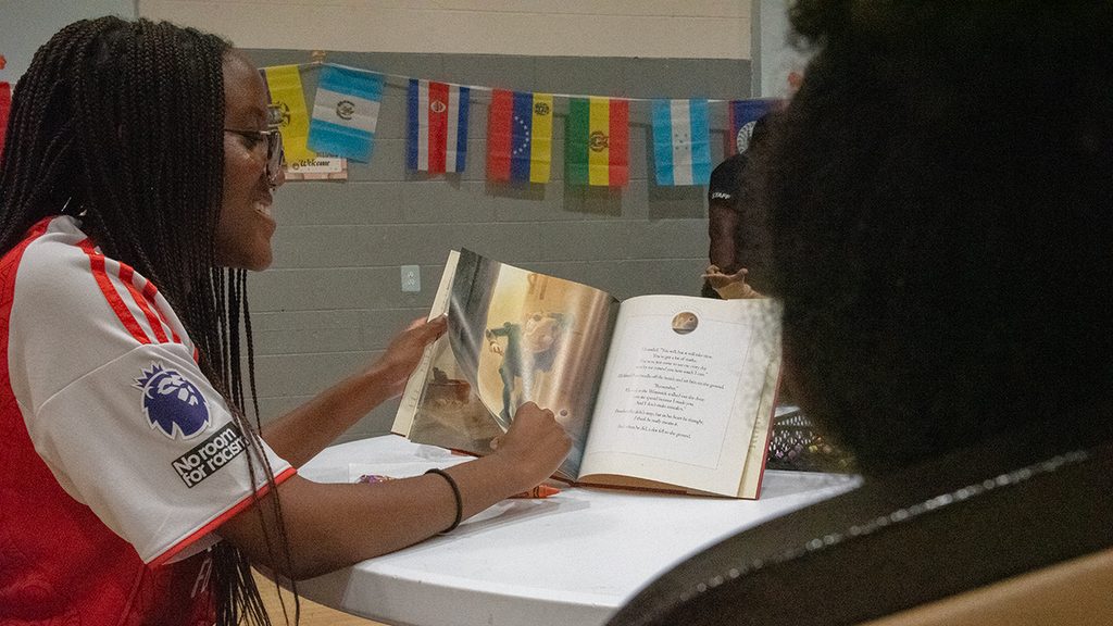 A student holding an open book at a table with children