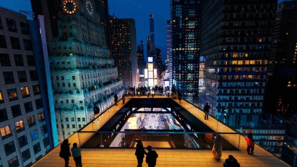A photo of people walking on an illuminated skywalk at night in Times Square