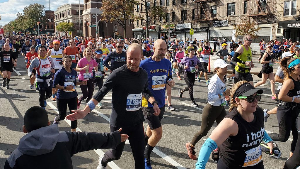 Runners in the NYC Marathon, one slapping hands with a viewer