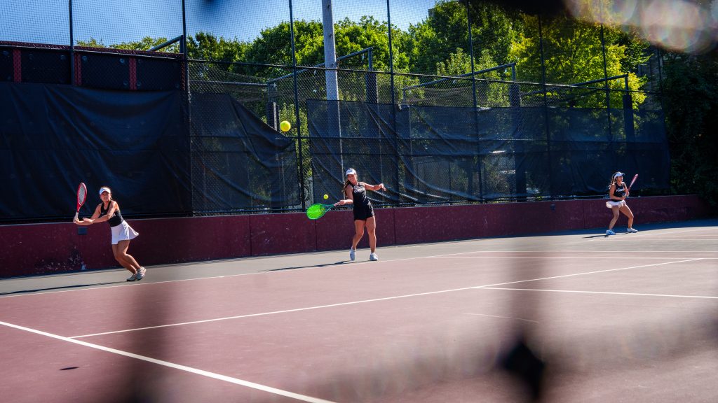 Three members of the women's tennis team hit balls on the court.